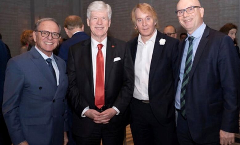 Four men in suits posing for a photo at a formal event, smiling for the camera in a hallway.