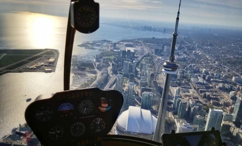 Cockpit view of a cityscape with the CN Tower and tall buildings, water to the left, taken from a small aircraft cockpit interior with gauges in the foreground.