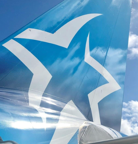 Close-up of a blue airplane tail fin with a large white star logo against a partly cloudy sky