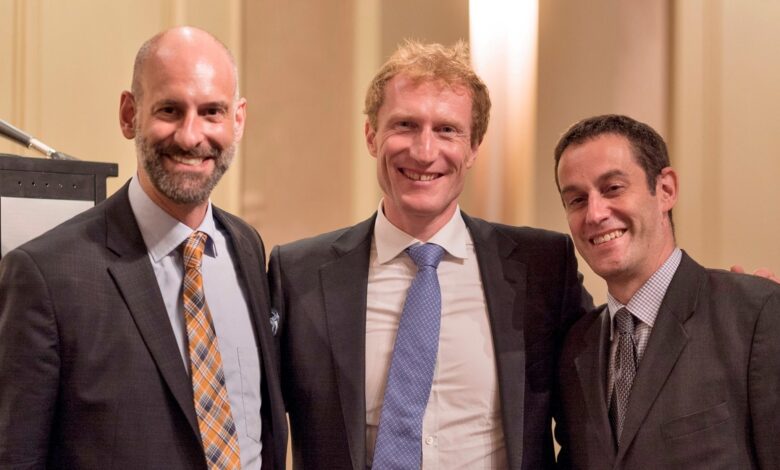 Three men in suits posing together and smiling at a formal event.