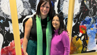 Two women smiling and posing together in front of a vibrant abstract mural.