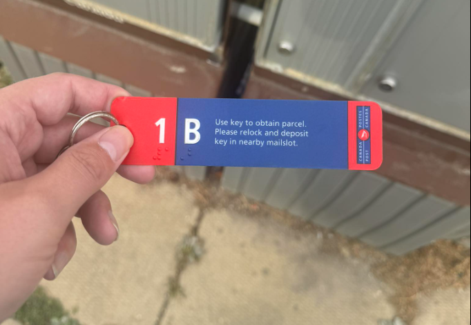 Hand holds a red-and-blue parcel key tag labeled '1 B' with instructions to use the key to obtain a parcel in the mailbox area.