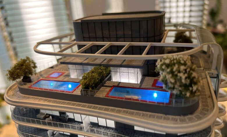 Miniature modern building complex with a rounded glass tower, elevated walkways, and blue water features.