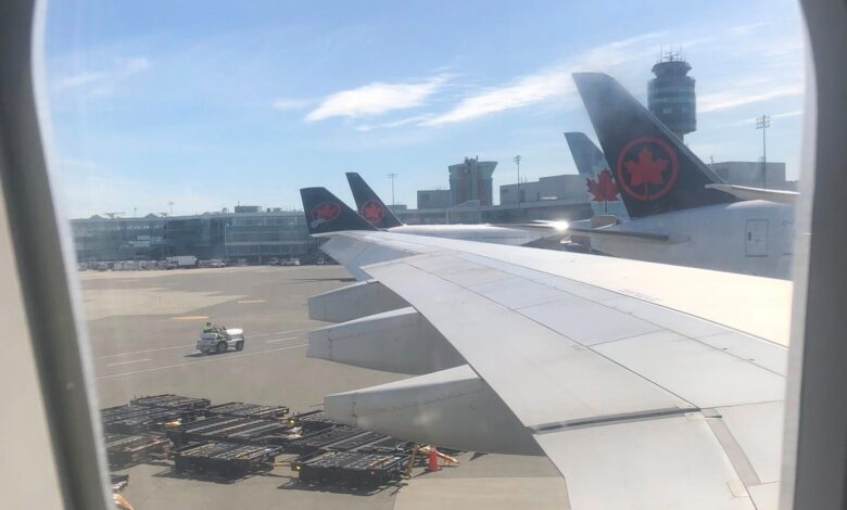 View of an aircraft wing and tail with Air Canada maple leaf logo at the gate, tarmac and airport buildings in the distance
