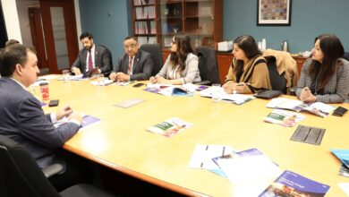 Group of professionals in a formal meeting around a large conference table, reviewing brochures and taking notes in an office setting.