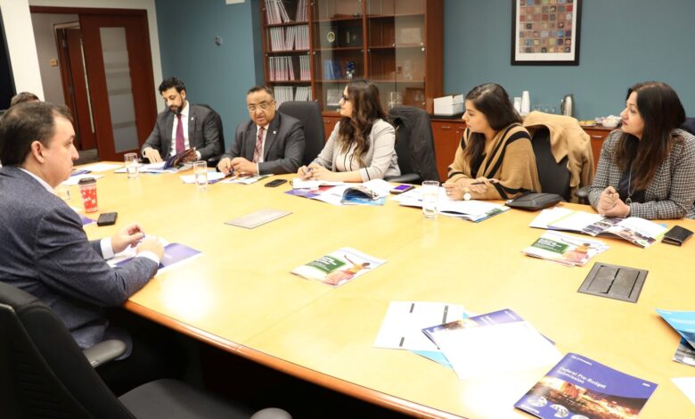 Group of professionals in a formal meeting around a large conference table, reviewing brochures and taking notes in an office setting.