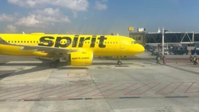Bright yellow Spirit Airlines plane parked at the gate on a sunny day, jet bridges in the background.