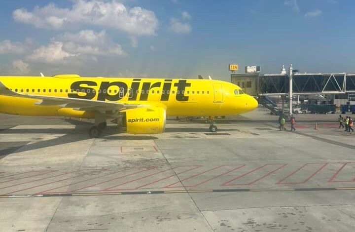 Bright yellow Spirit Airlines plane parked at the gate on a sunny day, jet bridges in the background.
