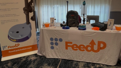 Table setup for FeedUp at a conference, featuring a branded banner and a table with medical feeding equipment and packets.