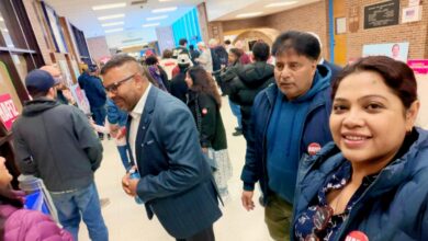 Smiling woman in a blue jacket takes a selfie in a crowded hallway at a campaign event; attendees wear red HAFIZ stickers.