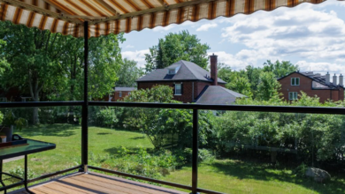 Wooden deck under an orange-and-white striped awning, with glass railing and a green suburban yard beyond.