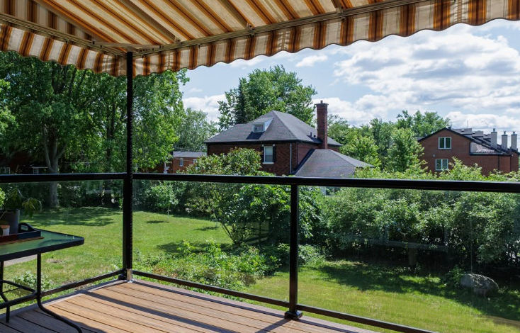 Wooden deck under an orange-and-white striped awning, with glass railing and a green suburban yard beyond.