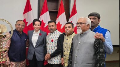 Group of six adults posing for a formal event, with Canadian flags in the background behind them.