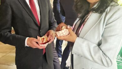 Two professionals in a suit and a light gray blazer share napkins at a social event, smiling at each other.