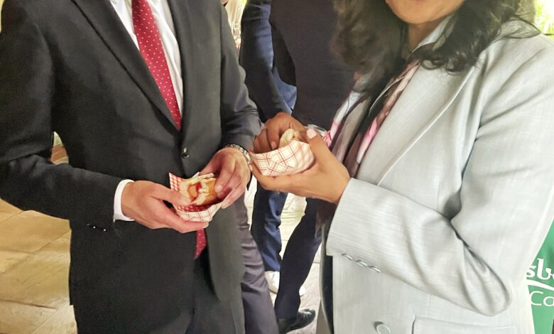 Two professionals in a suit and a light gray blazer share napkins at a social event, smiling at each other.