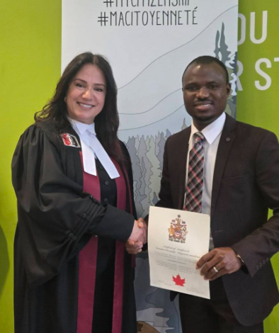 Two adults shake hands at a citizenship ceremony: a woman in academic robes and a man in a suit, holding a certificate with a red maple leaf; banner behind them displays '#MYCITIZENSHIP #MACITOYENNÉ' and Canada logos.