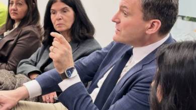 Man in a blue blazer speaks and gestures while seated with three colleagues in a business meeting.