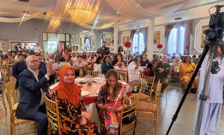Banquet hall filled with guests at round tables, ornate chandeliers, draped ceiling, and a camera on a tripod in the foreground.