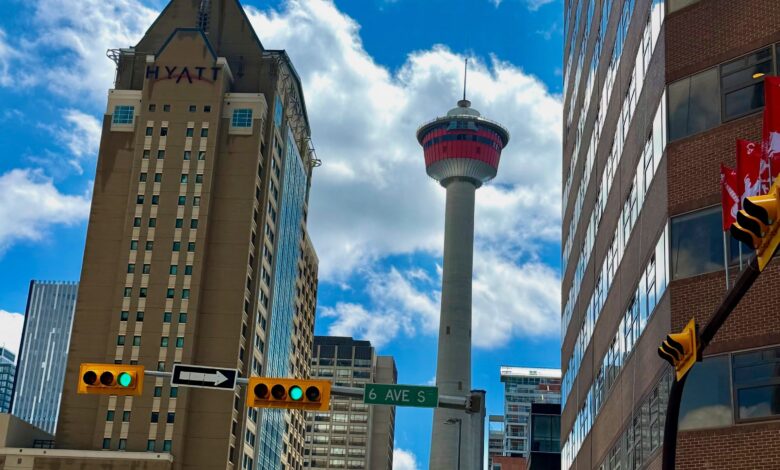 Urban street scene with tall beige and glass buildings, a distant tower, and a bright blue sky with clouds.