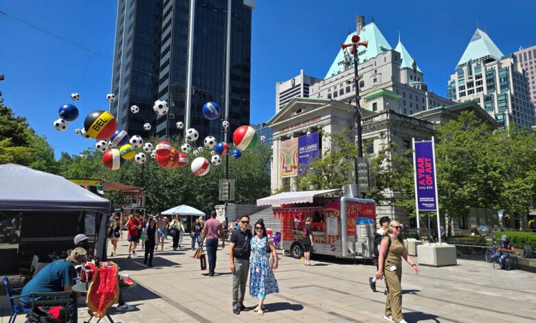 City square festival with hanging balloons, vendors, and people walking under a clear blue sky.
