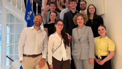 Group of young professionals posing on a curved staircase in a bright building, with a blue-and-white flag in the foreground.