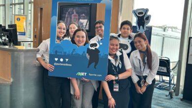 Group of smiling staff members posing with a blue promotional photo frame at a terminal check-in area, with A19 sign in the background.