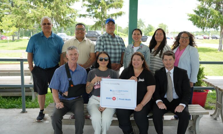 Group of adults posing for a photo outdoors, two rows, with a large certificate held by people in front.