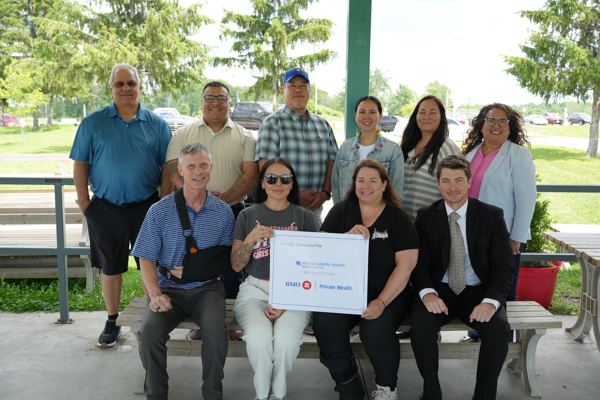 Group of adults posing for a photo outdoors, two rows, with a large certificate held by people in front.