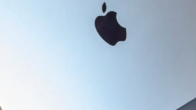 Closed silver Apple MacBook laptop angled on a gray-blue desk with the black Apple logo visible on the lid