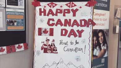 Poster reading 'Happy Canada Day' with maple leaf bunting, illustrated couple and children in red, and mountains at bottom (Canada Day celebration).