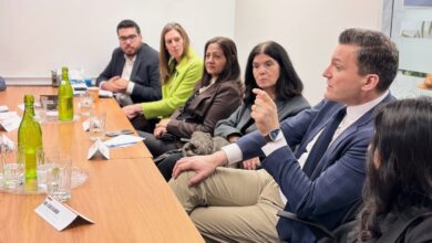 Group of professionals seated around a conference table, with one man in a blue suit speaking and gesturing.