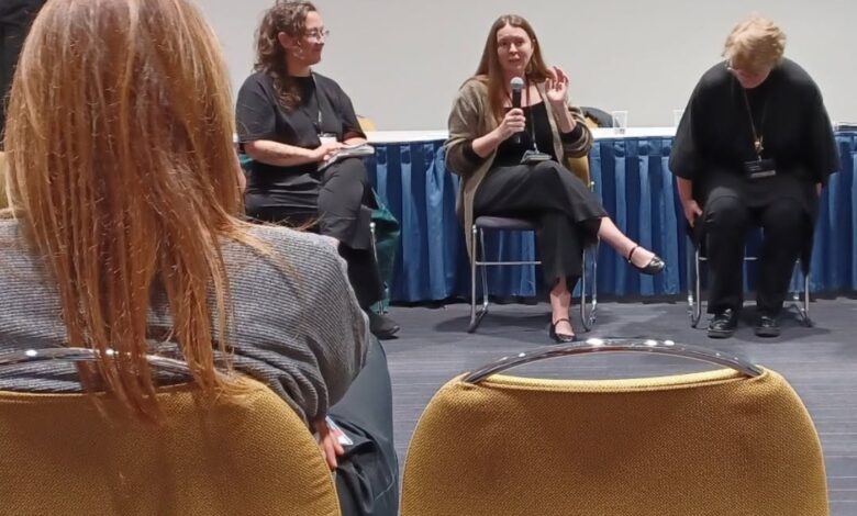 Panel discussion with four women seated on a stage; the center speaker holds a microphone and talks as the others listen.