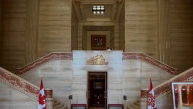 Grand marble stairway with red-patterned railings flanking a central doorway, flags displayed at the sides inside a grand hall.