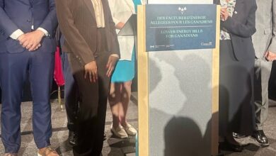 Group of diverse professionals posing on stage behind a podium promoting lower energy bills for Canadians (bilingual sign).