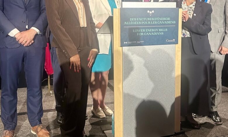 Group of diverse professionals posing on stage behind a podium promoting lower energy bills for Canadians (bilingual sign).