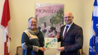 Two adults exchange a certificate in a formal room; flags flank them and a poster reading 'Le Montréalier' is on the wall behind.