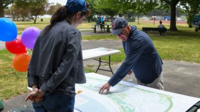 Two people study a large park map laid out on a table outdoors, with colorful balloons in the background.