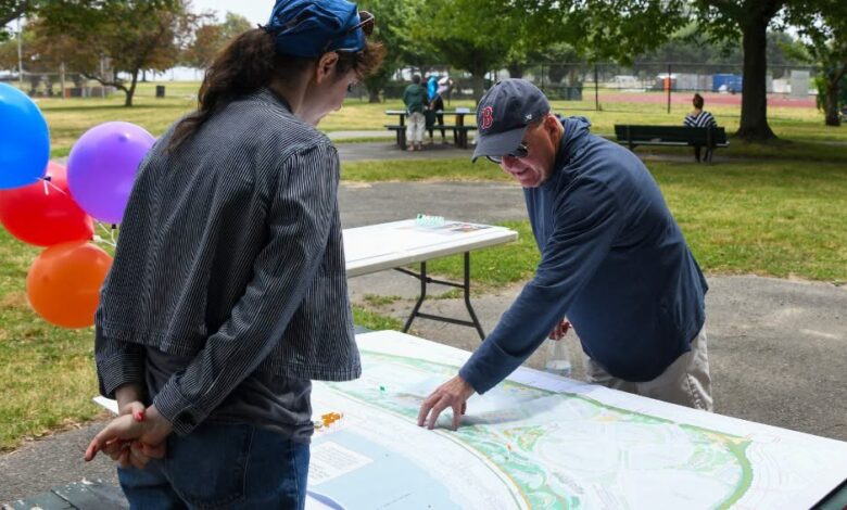 Two people study a large park map laid out on a table outdoors, with colorful balloons in the background.