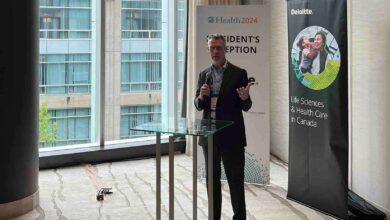 Male presenter in a suit speaks at a podium in a conference room, flanked by Health2024 and Deloitte banners.